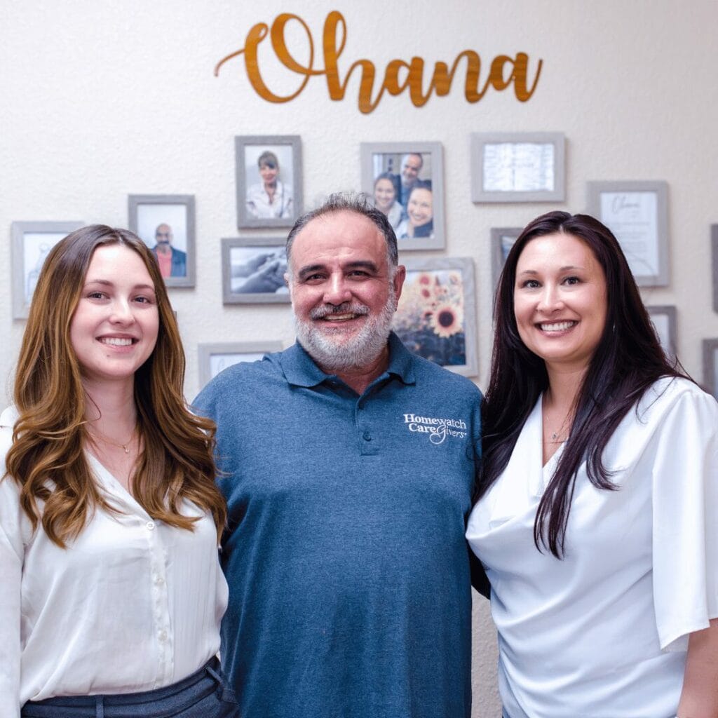two women and man standing in front of a wall of photos.