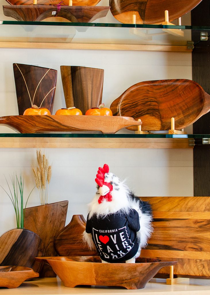display of wooden cutting boards and bowls with a toy rooster wearing an i love fair oaks shirt