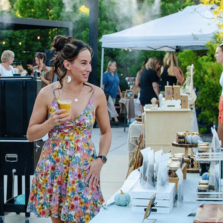 woman wearing a sundress holding a cocktail and shopping at a pop up market at shangri la a restaurant in fair oaks california
