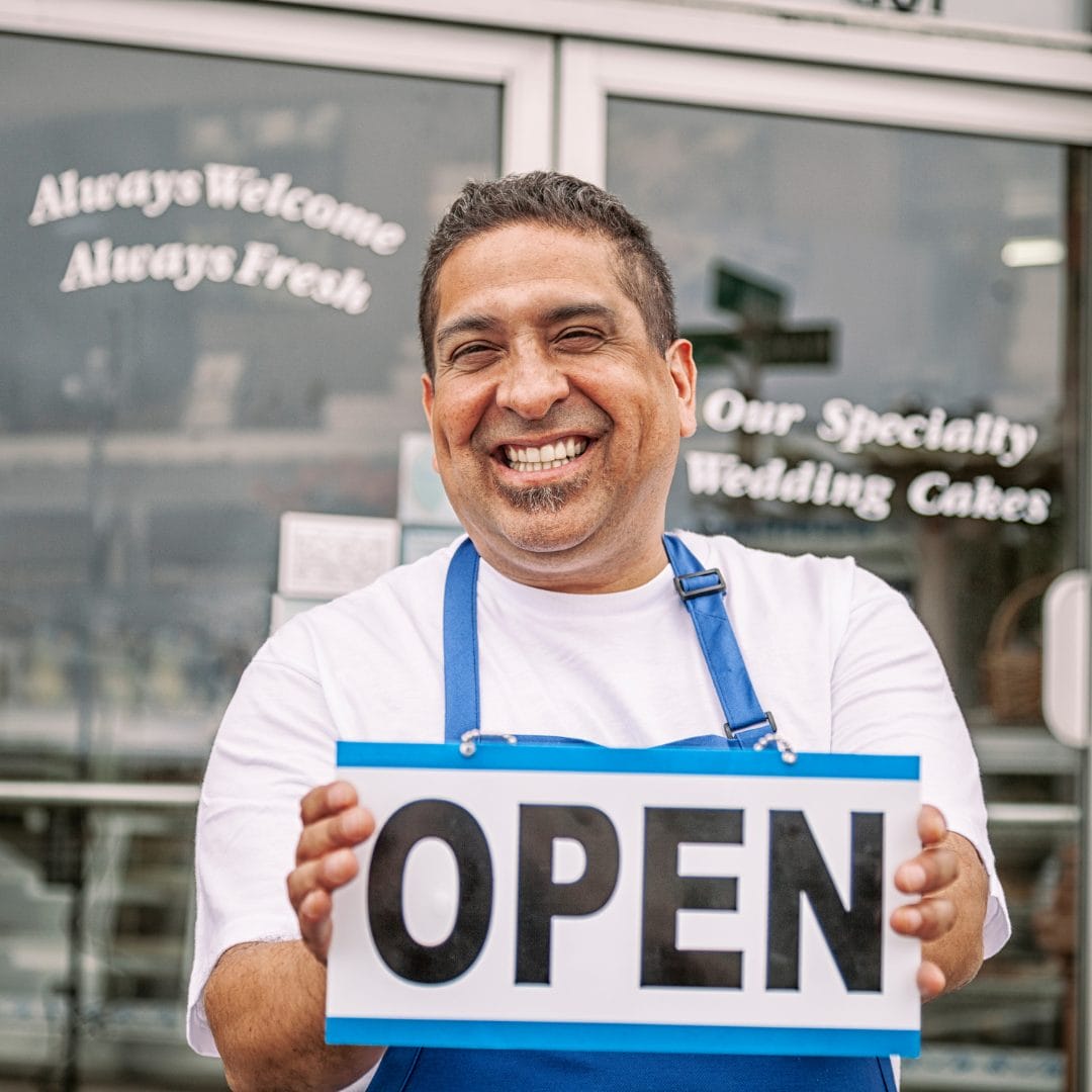 man holding an open sign in front of a bakery